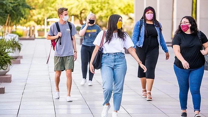 Students walk down an outdoor space on campus while smiling and wearing face coverings