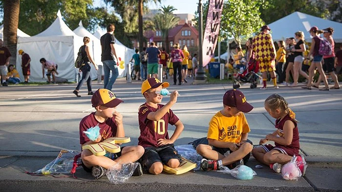 Kids sitting and eating cotton candy with ASU event going on in the background