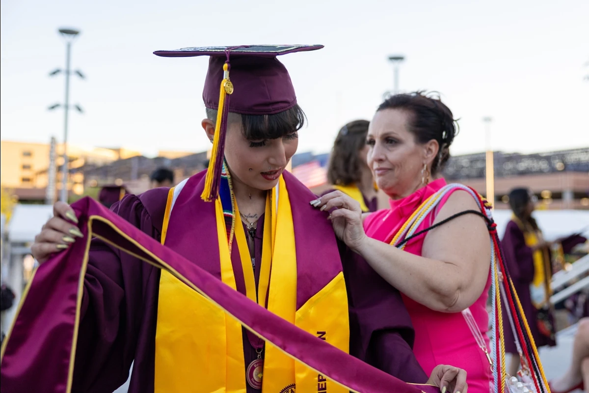 A mother helps her graduating student adjust her commencement regalia