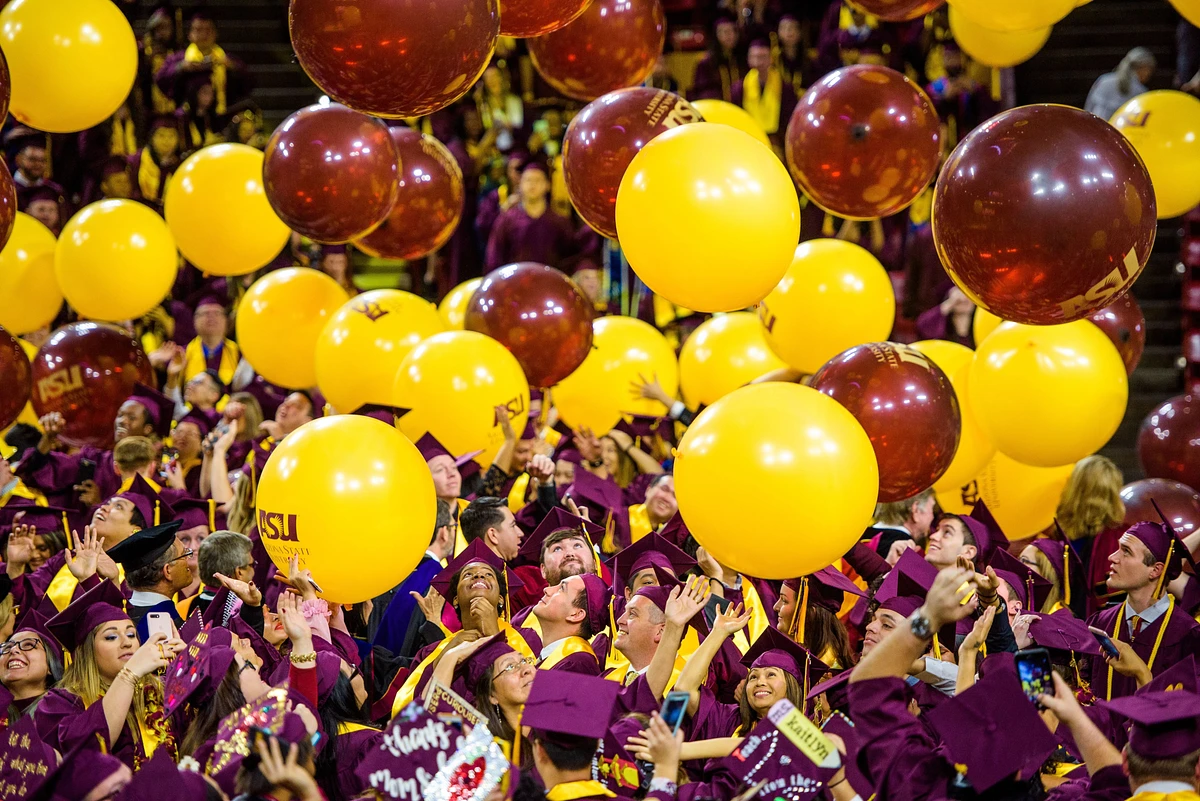 Graduates in caps and gowns celebrate by tossing yellow and maroon balloons at a commencement ceremony.