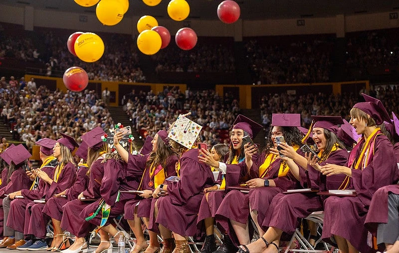 Graduates in caps and gowns joyfully celebrate by tossing balloons during a ceremony.